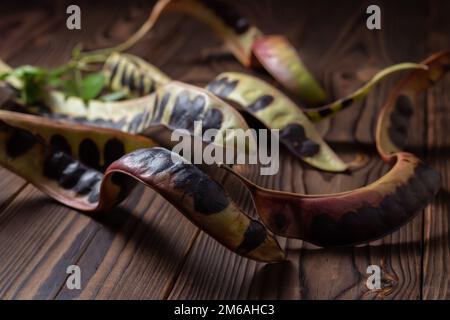 Akaziensamen. Schwarze Heuschrecke. Akazie auf Holzhintergrund. Stockfoto