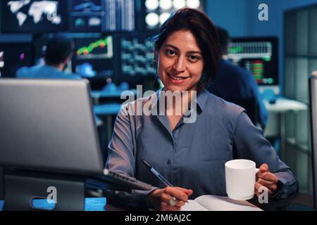 Junge Geschäftsfrau oder Maklerin, die am Finanzhandel mit einem Laptop-Computer arbeitet. Eine Investimentärin, die im Büro vor die Kamera schaut. Economy-Konzept. Hochwertiges Foto Stockfoto