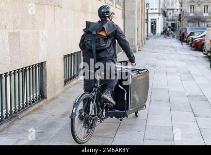 Rückansicht eines Kuriers, der auf einem Cargo Bike entlang der Stadt unterwegs ist, um ein Paket abzuliefern Stockfoto