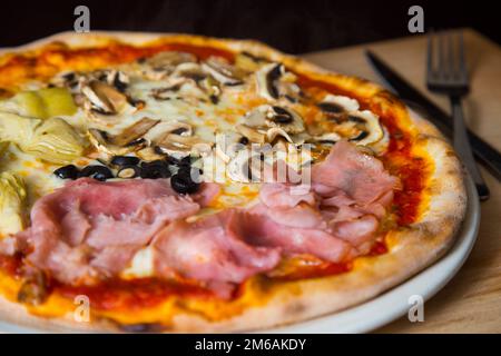 Four Seasons Pizza. Neapolitanische Pizza mit Tomatensoße, Käse, Schinken, Pilzen und Gemüse. Authentisches italienisches Rezept. Stockfoto