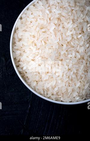 Schüssel mit ungekochtem weißem Reis auf schwarzem Hintergrund. Draufsicht. Nahaufnahme. Hintergrund und Textur. Stockfoto