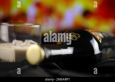 KIEW, UKRAINE - 4. MAI 2022 Baileys Original-Alkoholflasche auf Holztisch mit rotem Kamin im Hintergrund. Elite-Alkoholproduktion Stockfoto