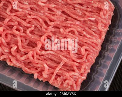 Ein Plastikbehälter mit Hackfleisch und Rindfleisch auf einer schwarzen Matte. Schließen. Stockfoto