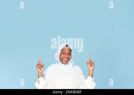 Sieh dir das an. Eine glückliche schwarze Frau in Hijab zeigt auf den Kopierbereich über ihrem Kopf und zeigt freien Platz für deine Anzeige Stockfoto