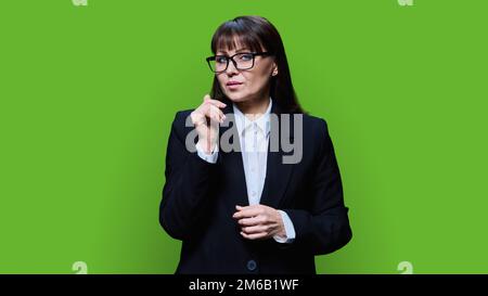 Porträt einer selbstbewussten, reifen Geschäftsfrau im schwarzen Anzug auf grünem Hintergrund Stockfoto