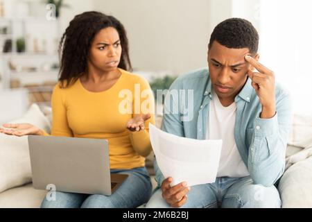 Wütende, unglückliche, afroamerikanische Millennials-Lady, die sich mit einem Laptop über Schulden und Rechnungen streitet Stockfoto