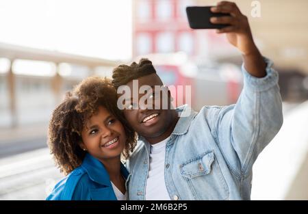 Glückliches Junges Schwarzes Paar, Das Selfie Auf Dem Smartphone Am Bahnhof Mitnimmt Stockfoto