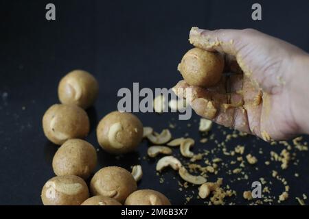 Herstellung von Moong dal laddu in Kugelform mit der Hand. Es ist eine proteinreiche, indische Süßigkeit, die aus Linsen, Mandeln und Jaggerie als Süßungsmittel hergestellt wird. Aufnahme mit Stockfoto