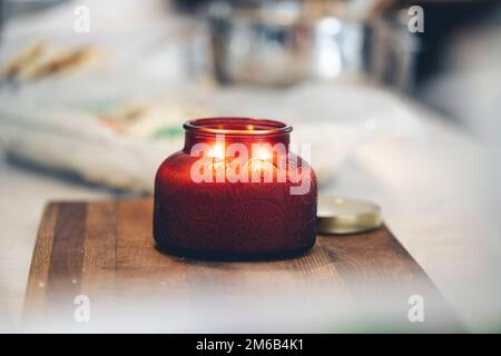 Eine Aromakerze in einem roten Glasgefäß auf einem Holzbrett. Stockfoto