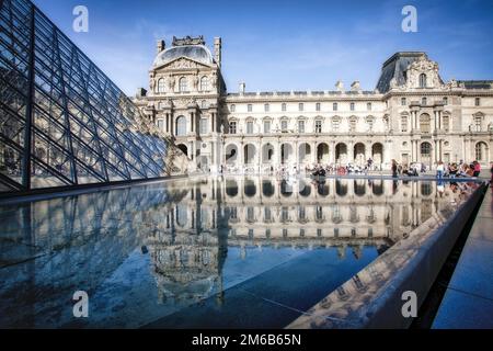 Touristen treffen sich in der Nähe eines reflektierenden Pools im Innenhof des Louvre in Paris, Frankreich. Stockfoto