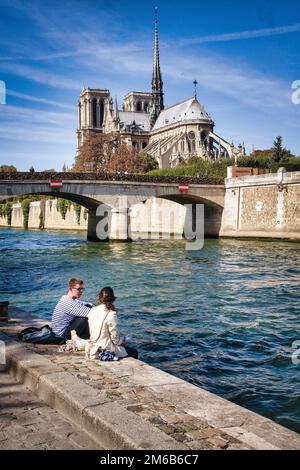 Ein paar genießt das ideale Wetter entlang der Seine unterhalb der Pont Archeveche und Notre Dame.  Paris, Frankreich. Stockfoto