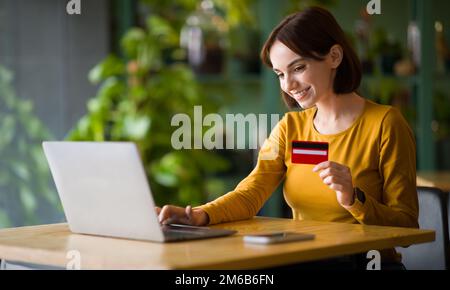 Junge Frau mit Kreditkarte und Laptop im Café Stockfoto