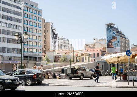 Street Art in der Nähe von Athen Central Municipal Market, Monastiraki, Athen, Griechenland. Gebäude umgeben eine Straße mit Autos und Menschen. Die Gebäude verfügen über en Stockfoto