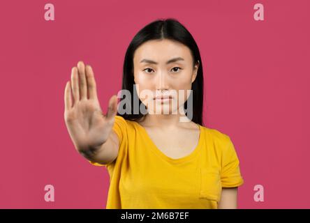 Eine junge japanische Dame, DIE AUFHÖRT, eine Abstoßungsgeste zeigt, ihre negative Einstellung ausdrückt, rosa Hintergrund Stockfoto
