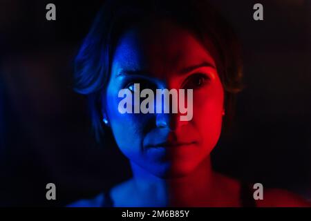 Das Gesicht einer jungen Frau in blauem und rotem Neonlicht auf dunklem Hintergrund. Stockfoto