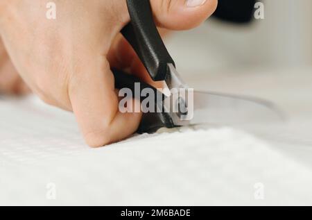 Arbeiten Sie zu Hause. Kleine Unternehmen. Eine Schneiderin schneidet einen weißen Stoff auf den Tisch. Nahaufnahme. Stockfoto