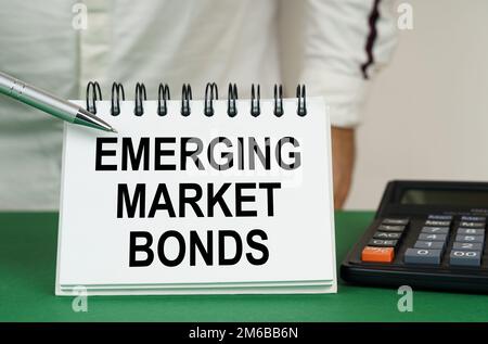 Geschäftskonzept. Auf einer grünen Oberfläche befindet sich ein Taschenrechner, ein Mann zeigt mit einem Stift auf ein Notizbuch mit der Aufschrift "Emerging Market Bonds" Stockfoto