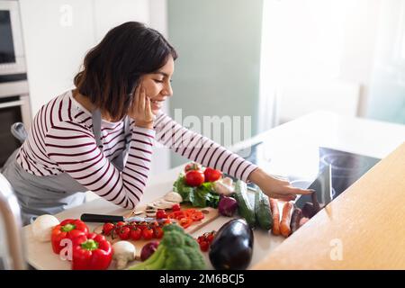 Eine Frau aus dem Nahen Osten, die zu Hause kocht und ein digitales Tablet benutzt Stockfoto