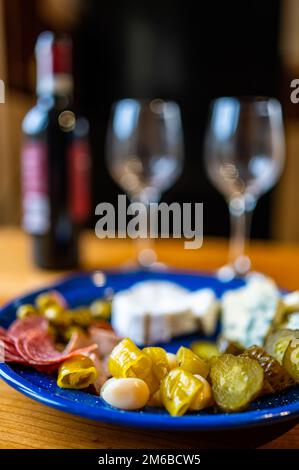 Vorspeisen, zubereitet mit einer Flasche Rotwein. Ein Teller gefüllt mit verschiedenen Käsesorten, Oliven, Paprika, Wurst, Knoblauch und Gurke und einem bot Stockfoto