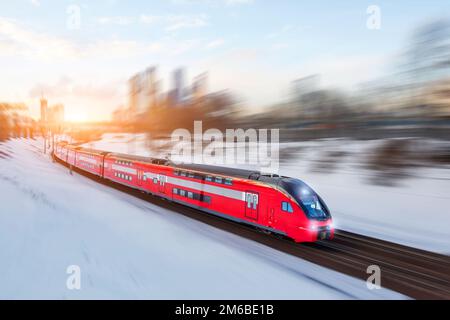 Eisenbahn in Bewegung bei Sonnenuntergang. Bahnhof mit Bewegungsunschärfe-Effekt gegen den farbenprächtigen blauen Himmel. Reisen, Eisenbahntourismus. Verschwommene Eisenbahn Stockfoto