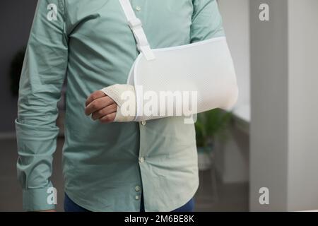 Ein Mann trägt einen Verband und eine Schlinge nach der Operation am Arm mit einer Gelenkluxation Stockfoto