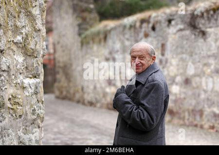 Älterer Mann, der an den Stadtmauern einer historischen deutschen Stadt steht und über die Schulter blickt Stockfoto