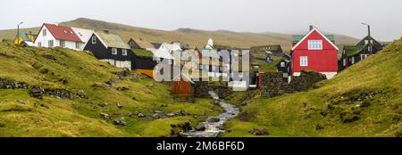 Der Bach, der an Häusern mit tuf-Dächern in Mykines vorbeiführt Stockfoto