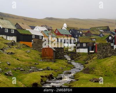 Der Bach, der an Häusern mit tuf-Dächern in Mykines vorbeiführt Stockfoto