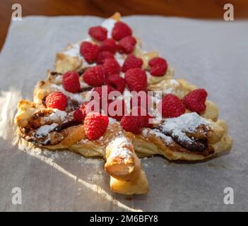 Schokoladen-Nutella-Blätterteig-Dessert mit Himbeeren in Form eines Weihnachtsbaums. Stockfoto