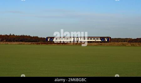 Auf dem Rasen befindet sich ein Zug, ein Zug aus dem Norden Nr. 156 423 überquert Bescar Moss, vorbei an einem Feld, auf dem das Rasen gewachsen ist und noch angehoben werden muss. Stockfoto