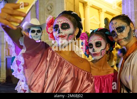 Drei junge Frauen, die als Catrinas verkleidet sind, machen ein Selfie bei der alljährlichen Catrina Parade von Merida, um den Tag der Toten (Día de los Muertos) in Yucatan, Mexiko, zu feiern Stockfoto