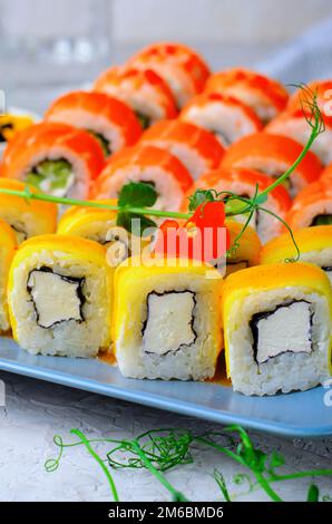 Sushi-Brötchen mit Lachs, Garnelen und Mango auf hellblauem Hintergrund, japanische Küche, asiatische Küche Stockfoto