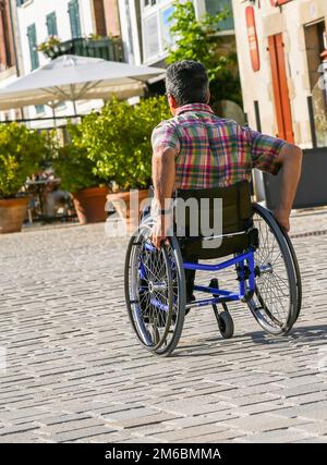 Behinderter Mann rollt die Straße hinunter in seinem Rollstuhl Stockfoto