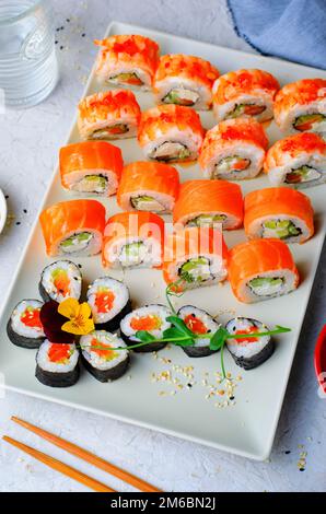 Sushi-Brötchen mit Lachs und Garnelen auf hellblauem Hintergrund, blumige Maki Sushi Rolls, japanische Küche Stockfoto