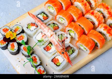 Sushi-Brötchen mit Lachs und Garnelen auf hellblauem Hintergrund, blumige Maki Sushi Rolls, japanische Küche Stockfoto