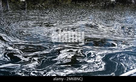 Schaum- und Blasenlinien drehen sich, um ein wunderschönes Muster zu erzeugen, wo sich zwei Flüsse treffen. Stockfoto