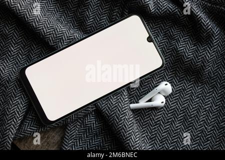 Telefon mit kabellosen Kopfhörern mit weißem Bildschirm auf grauem Stoff und Technologie Stockfoto