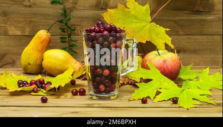 Stillleben Im Herbst. Preiselbeeren in einem Glas mit Herbstblättern, Äpfeln und Birnen. Stockfoto