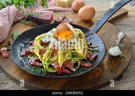 Herzhafte Spaghetti mit Südtiroler Speck und Eigelb, serviert in einer eisernen Bratpfanne Stockfoto