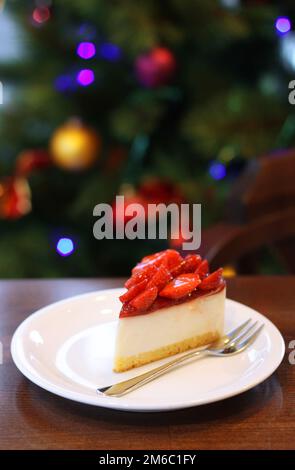 Frische Erdbeer Käsekuchen. Selektiven Fokus an der oberen Vorderkante des Kuchens. Weihnachtsbaum im Hintergrund Stockfoto