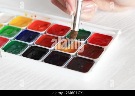 Malvorgang mit Aquarellen, einer Palette und einem Pinsel in der Hand Stockfoto