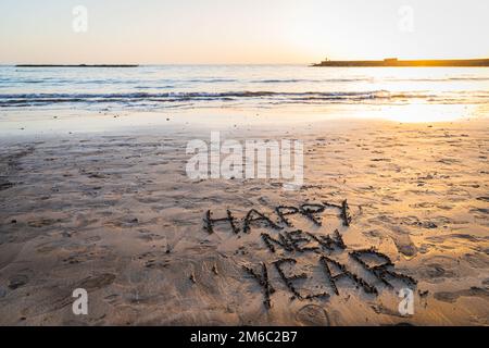 "Frohes neues Jahr" am Strand während des Sonnenuntergangs geschrieben, Foto mit Kopierbereich Stockfoto