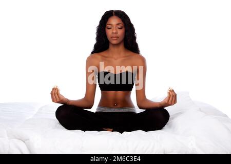 Schöne Frau, die in Lotus-Yoga-Pose auf dem Bett sitzt Stockfoto