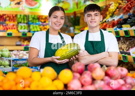 Positiv lächelnde Verkäuferin und Verkäufer in der Schürze, die frisches Obst im Geschäft anbietet Stockfoto