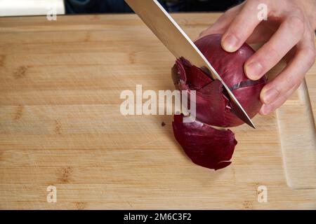Blick auf Händen eines Mannes hacken und eine frische rote Zwiebel schälen, mittags ein Bambus Schneidebrett. Stockfoto