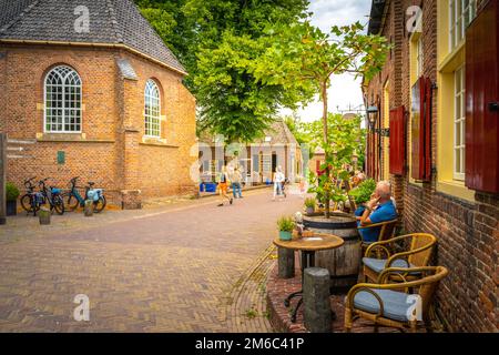 Ein Blick auf die Straße von Leuten, die im Café sitzen und andere laufen in der Nähe von alten Architekturen in Bronkhorst, Niederlande Stockfoto