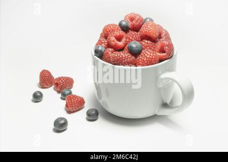 Himbeeren und Heidelbeeren in einem großen Becher auf weißem Hintergrund Stockfoto