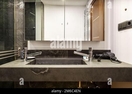 Kleines Badezimmer mit schwarzen Marmorablageflächen mit integriertem Waschbecken, Schrank mit Glastüren und Edelstahlhähnen Stockfoto