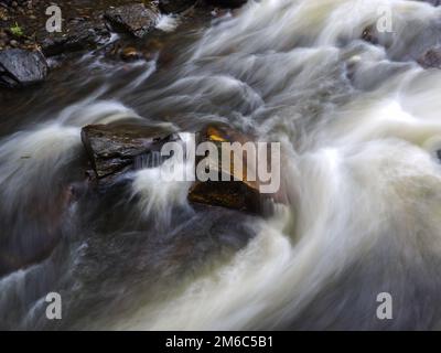 Starke Strömung im Fluss vorbei an Felsen, lange Exposition Stockfoto