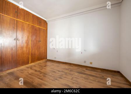 Leeres Zimmer mit eingebautem Kleiderschrank mit alten Sapelentüren und dunklen Holzböden Stockfoto